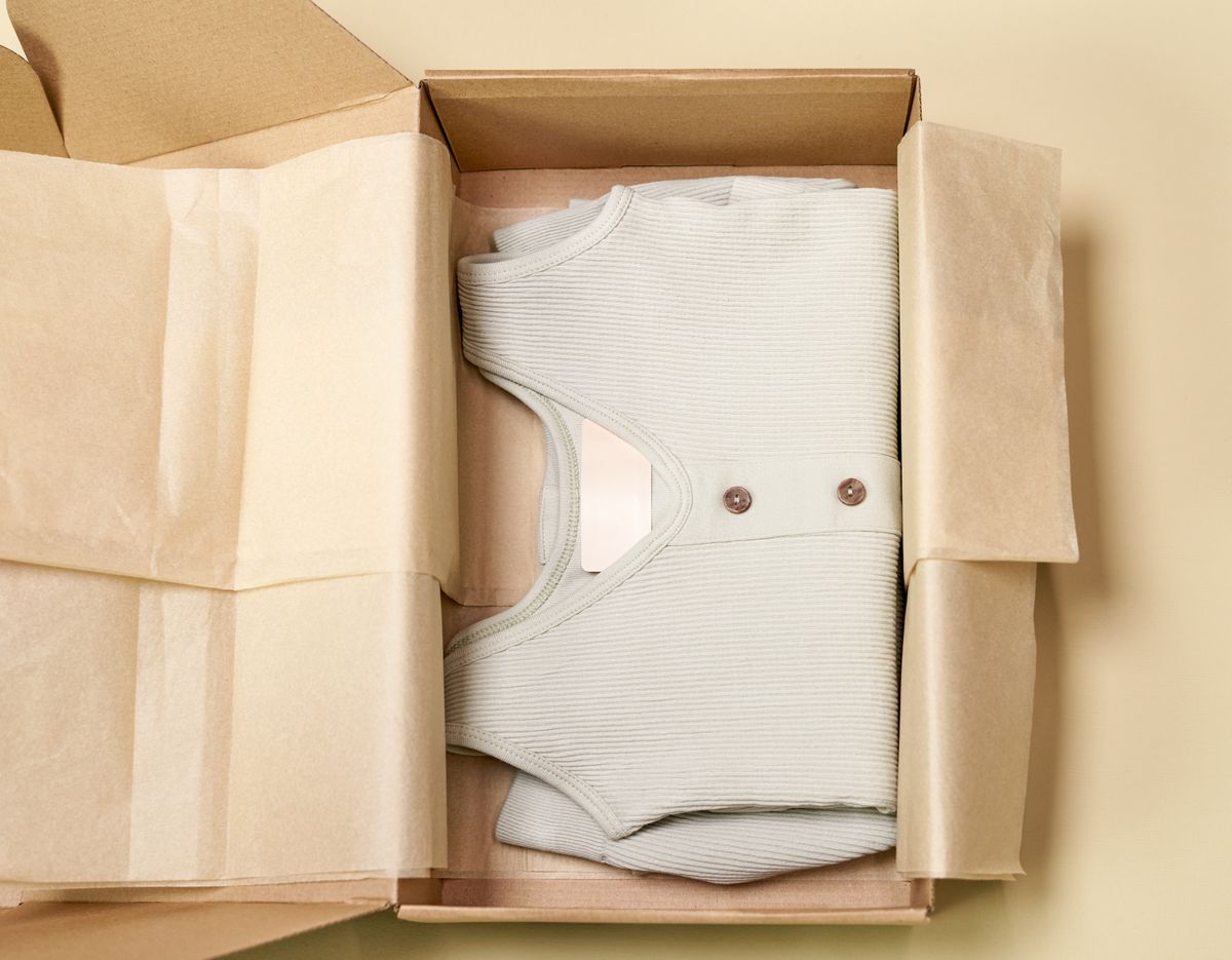 A knit cardigan folded in tissue inside a kraft box